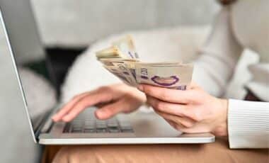 A Woman With A Handful Of Cash Payments In Front Of A Computer Screen