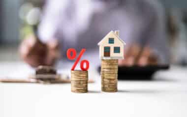 Miniature House On Stacked Coins With Percentage Symbol Representing Mortgage Rates And Property Investment