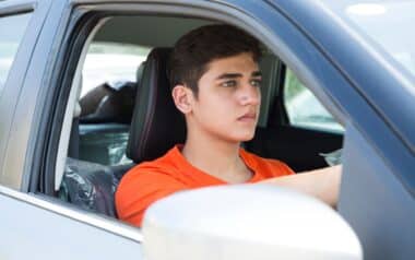 A young man, sitting in the driver's seat of a car with a focused and serious expression.