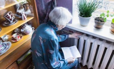 Woman in front of a heating radiator holding a notice of winter fuel payment.