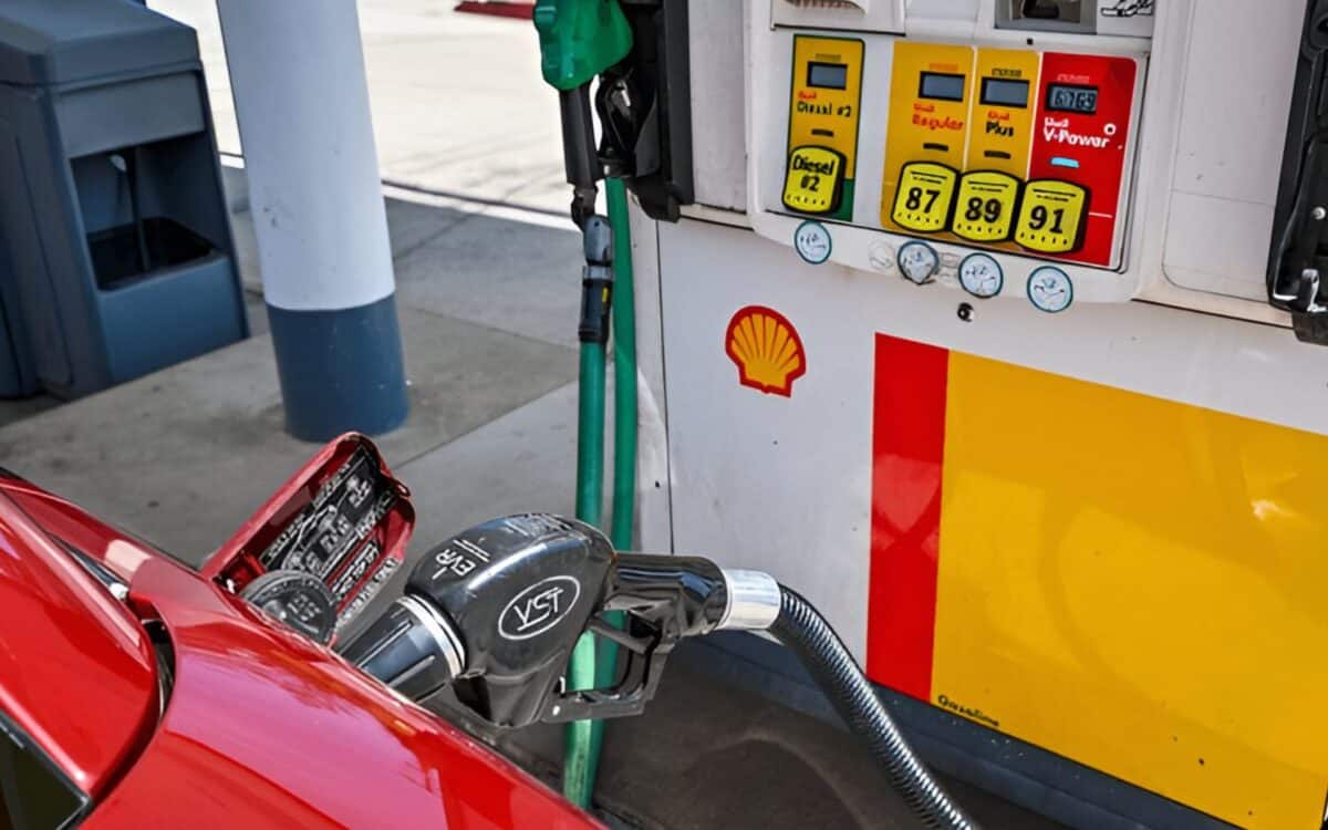 gas pump at a Shell gas station, with a fuel nozzle inserted into the tank of a red vehicle