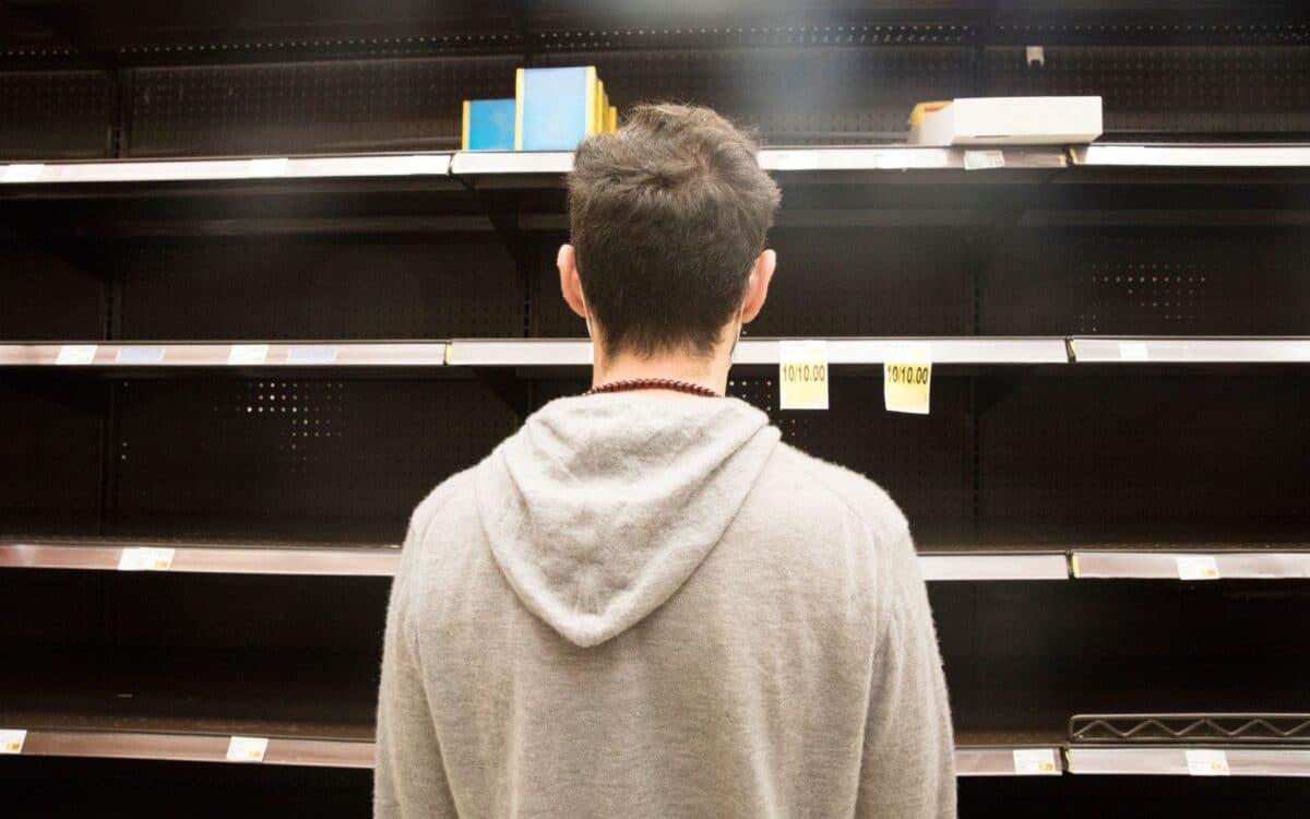 Man shopping in supermarket out-of-stock, looking at empty shelves.