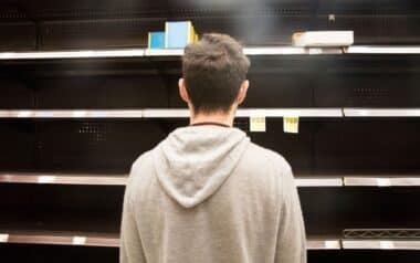 Man shopping in supermarket out-of-stock, looking at empty shelves.