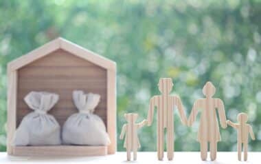 Wooden family figures beside a house model with money bags