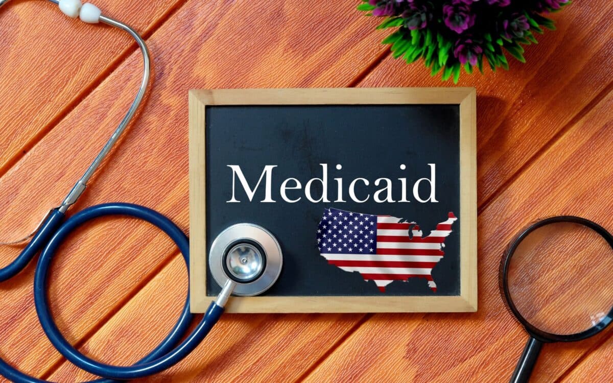 Top view of stethoscope,magnifying glass,plant and blackboard written with Medicaid on wooden background. Health concept.