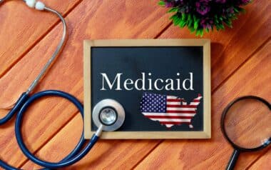 Top view of stethoscope,magnifying glass,plant and blackboard written with Medicaid on wooden background. Health concept.