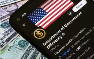 A smartphone shows the DOGE agency profile over U.S. dollar bills, symbolizing government savings and taxpayer refunds.