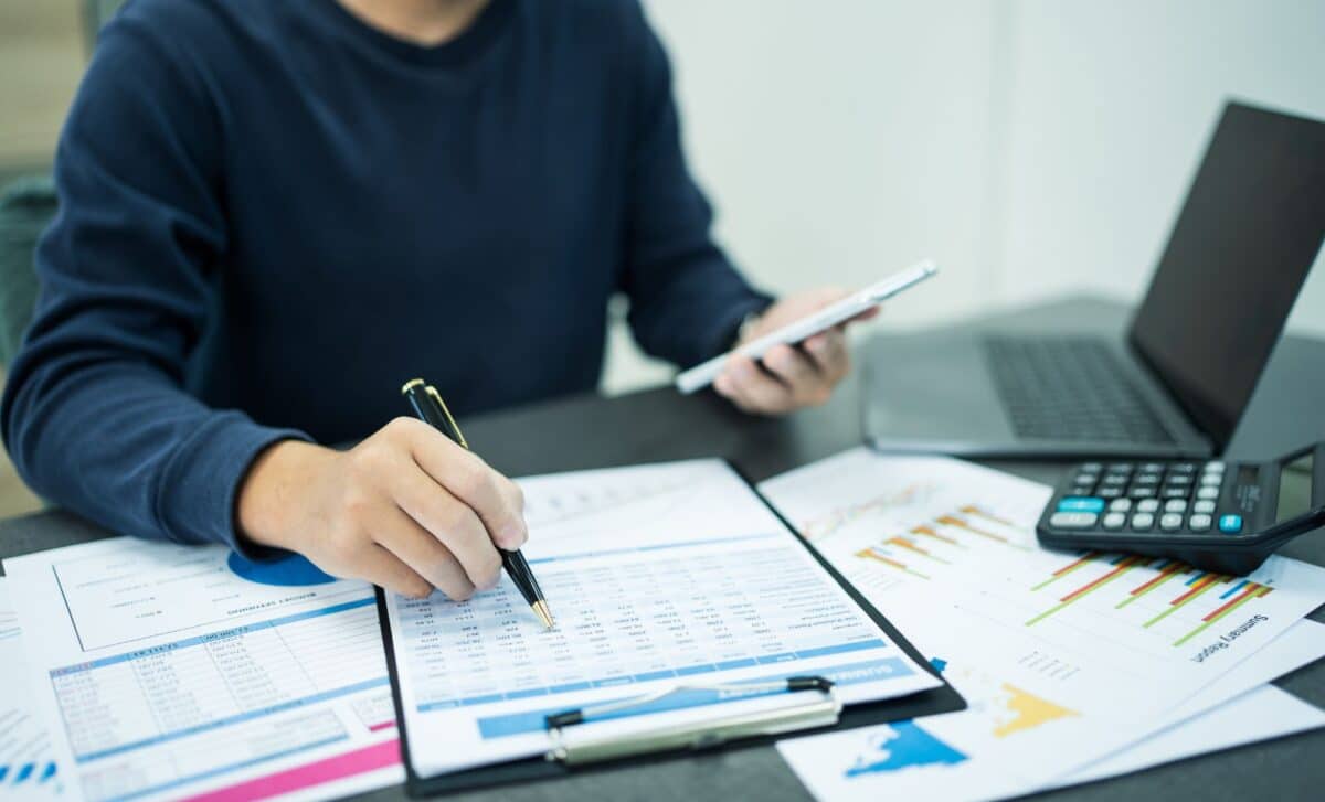 Man working, with phone in hand, computer and calculator on desk along with some documents