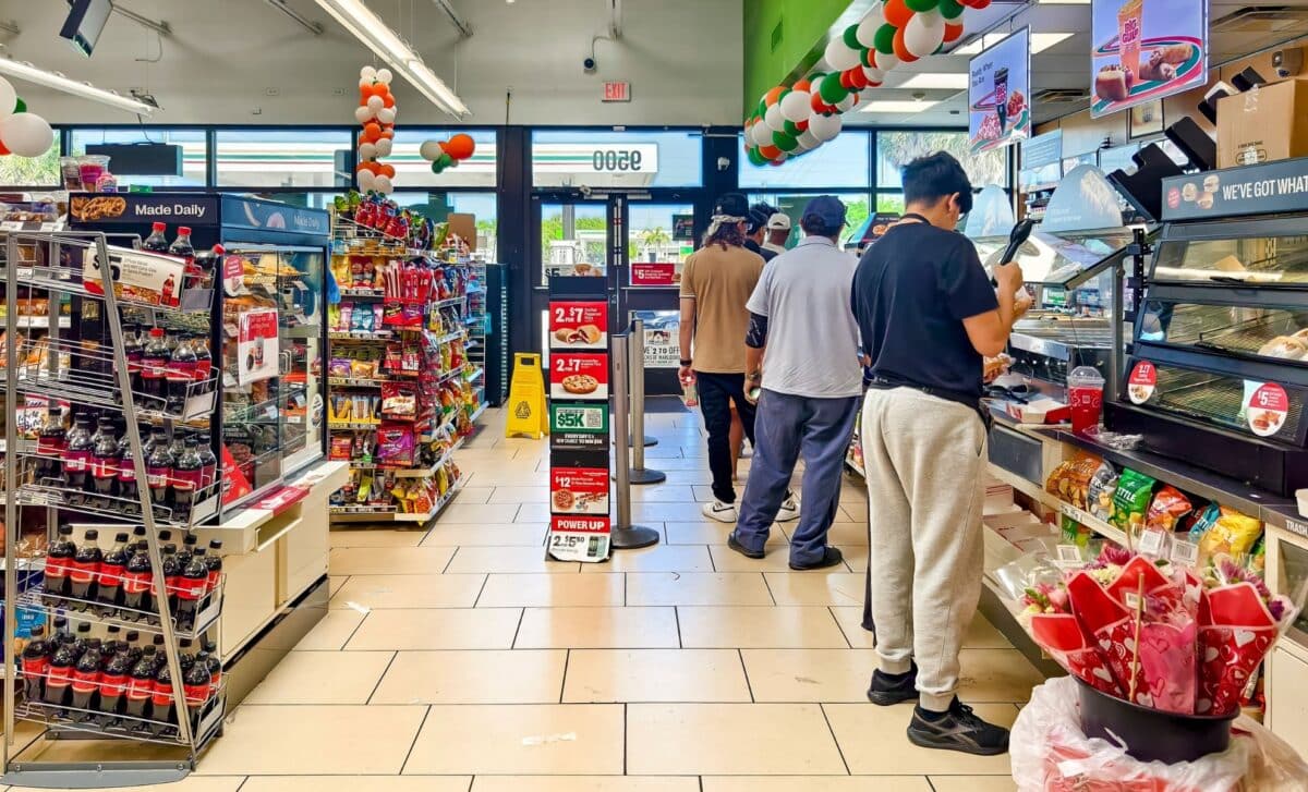 Inside a 7-Eleven convenience store viewing customers queuing and various products organized on shelves within the vibrant retail environment.