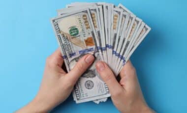 Two Hands Holding U.S. Dollar Bills Against a Light Blue Background