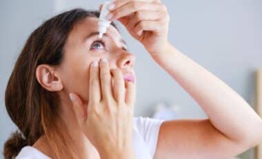 Woman applying eye drops to her eye while looking upward